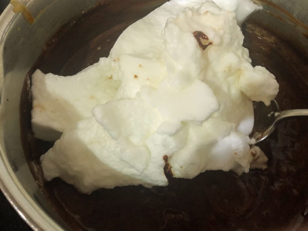 Whipped egg whites being added to melted chocolate to finish off a chocolate mousse.