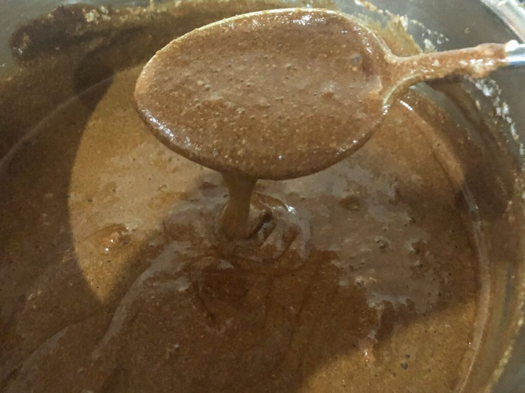 A chocolate caramel mousse dropping from a spoon with a double cream like texture before being added to pots.