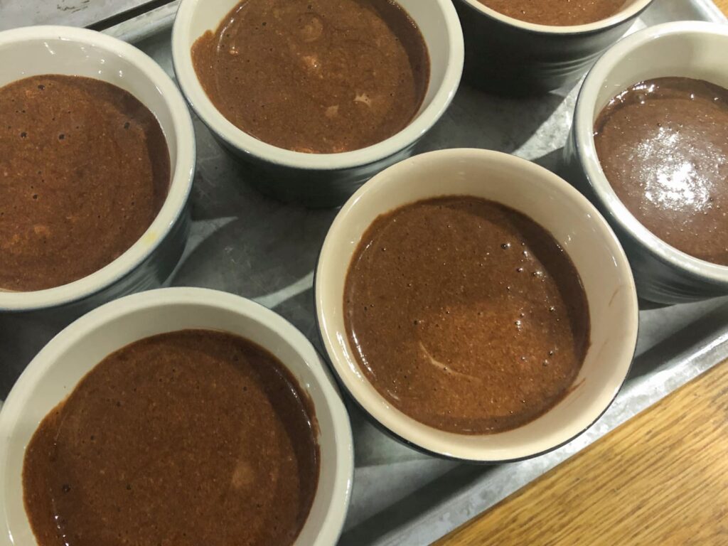 6 small pots of chocolate mousse in a metal tray ready for the fridge to chill and set.