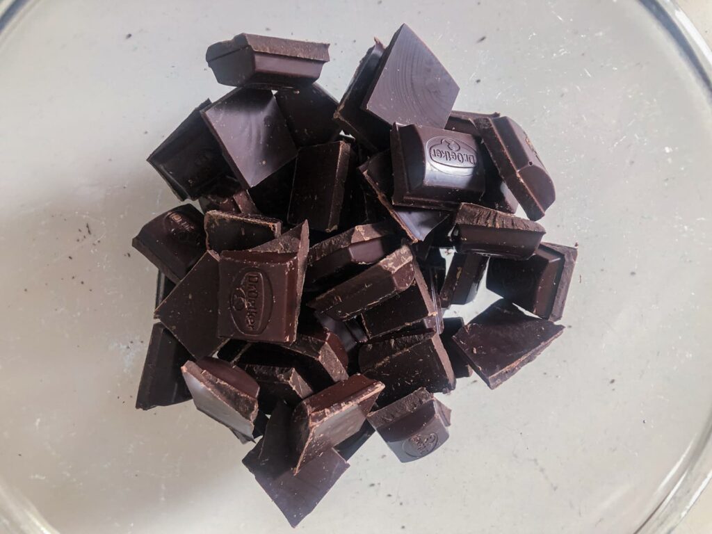 Dark chocolate broken into small pieces in a glass bowl.