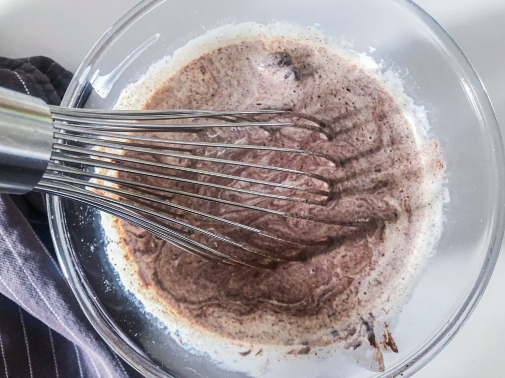 A whisking mixing warmed double cream and dark chocolate in a bowl.