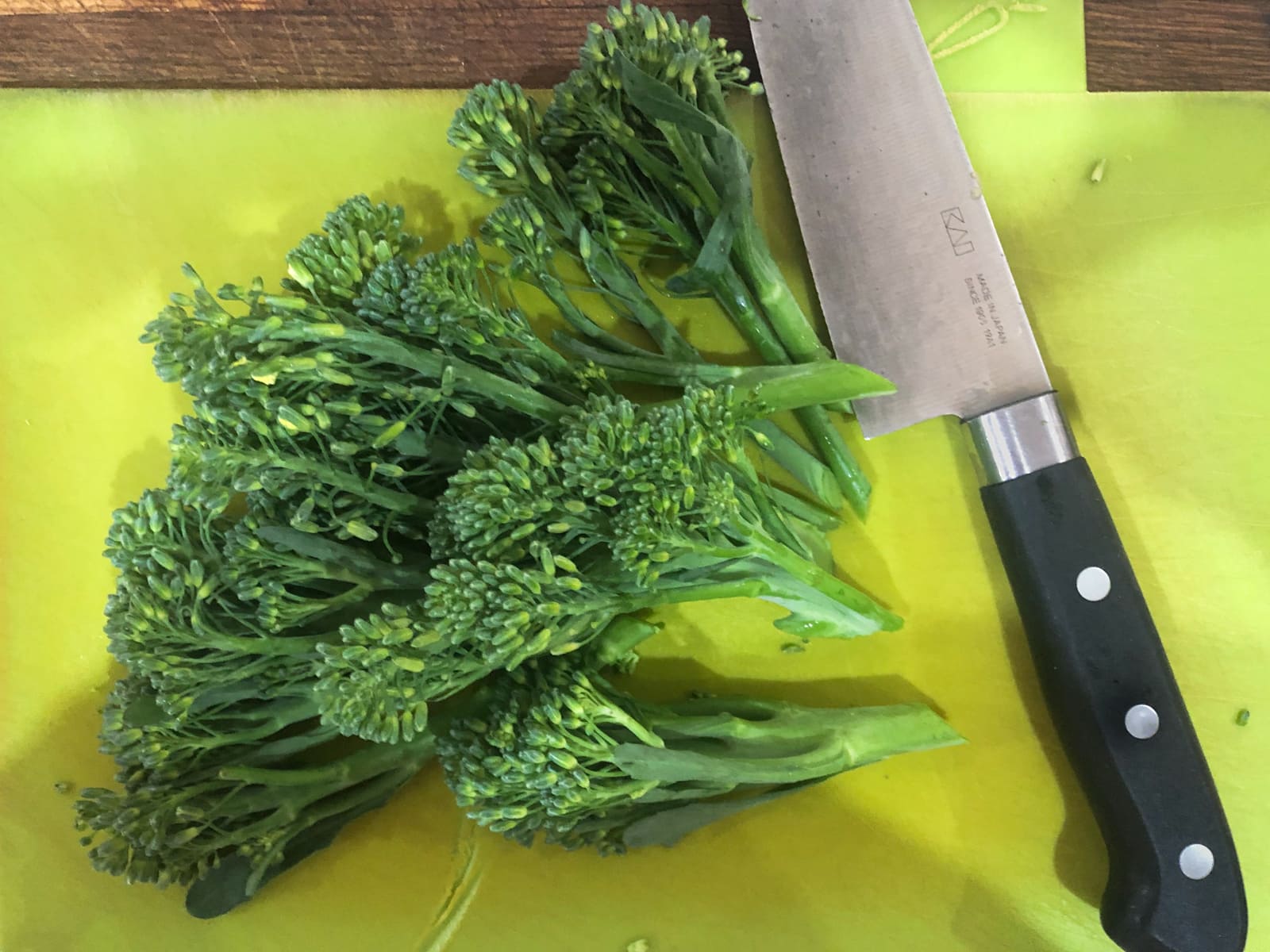 Stems of tenderstem broccoli on a green chopping board with a chefs knife to the right hand side.