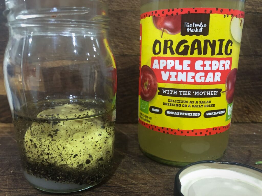A salad dressing being made in a jam jar and a bottle of apple cider vinegar to the right sat on a wooden surface.