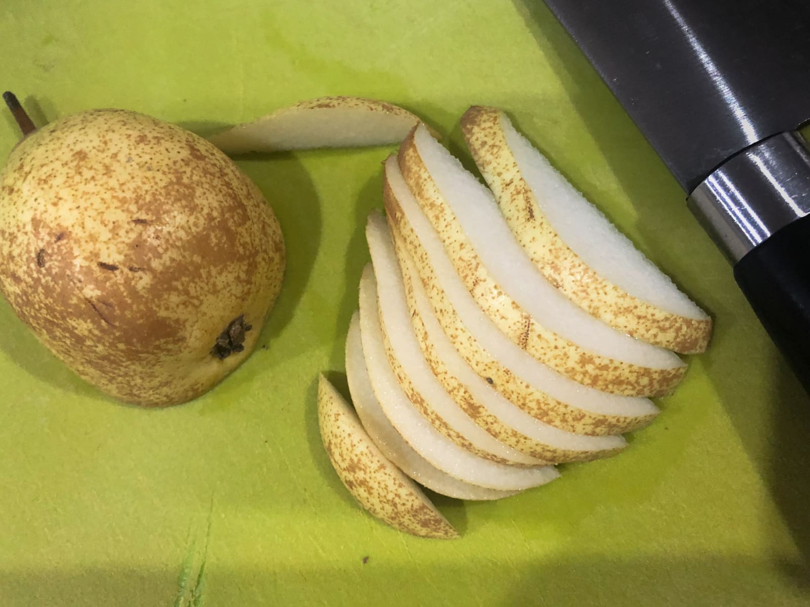 A pear sliced lengthways on a green chopping board before being added to a salad.