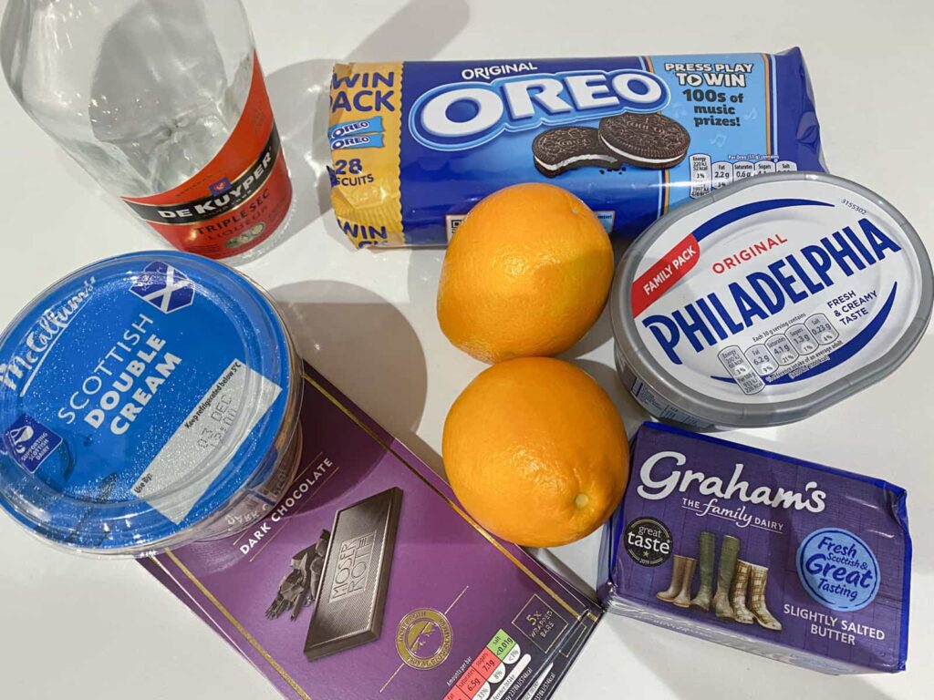 Ingredients for a no bake chocolate orange cheesecake consisting of dark chocolate, butter, oreo cookies, cream cheese, double cream and oranges and orange liqueur.