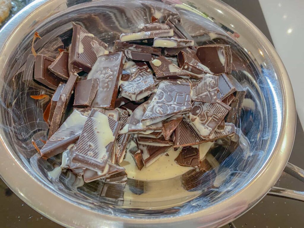Dark chocolate pieces and double cream in a glass bowl melting over a pan of simmering water.
