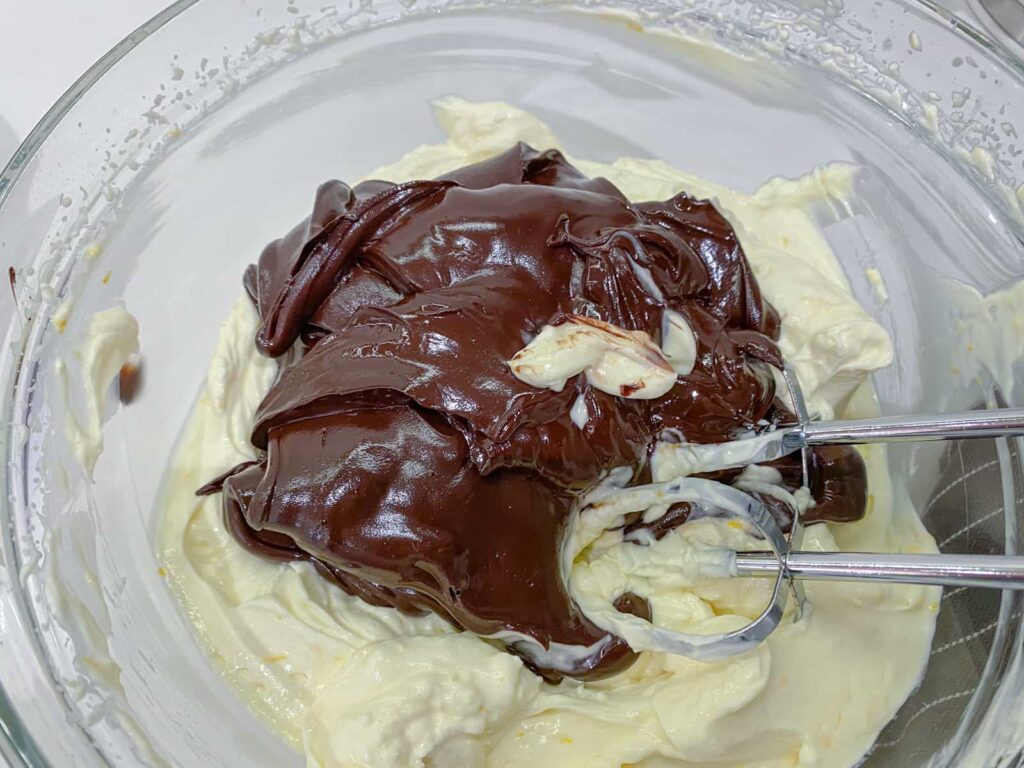 Sweetened cream cheese and melted chocolate being whisked together in a glass bowl.