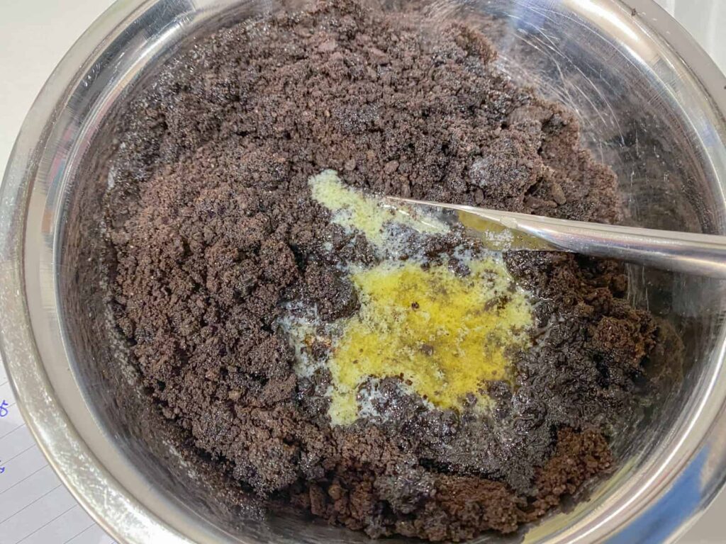 Oreo cookie crumbs with melted butter in a bowl.