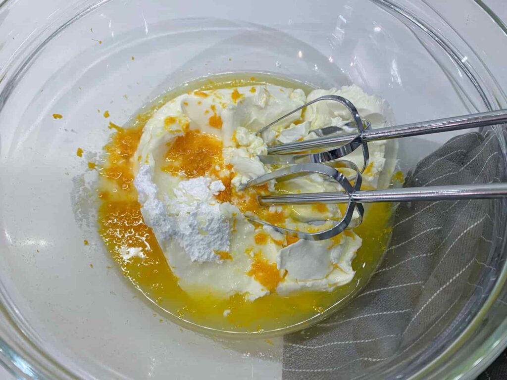 Cream cheese, sugar about to be mixed with orange juice, zest and liqueur as the base of a cheesecake.