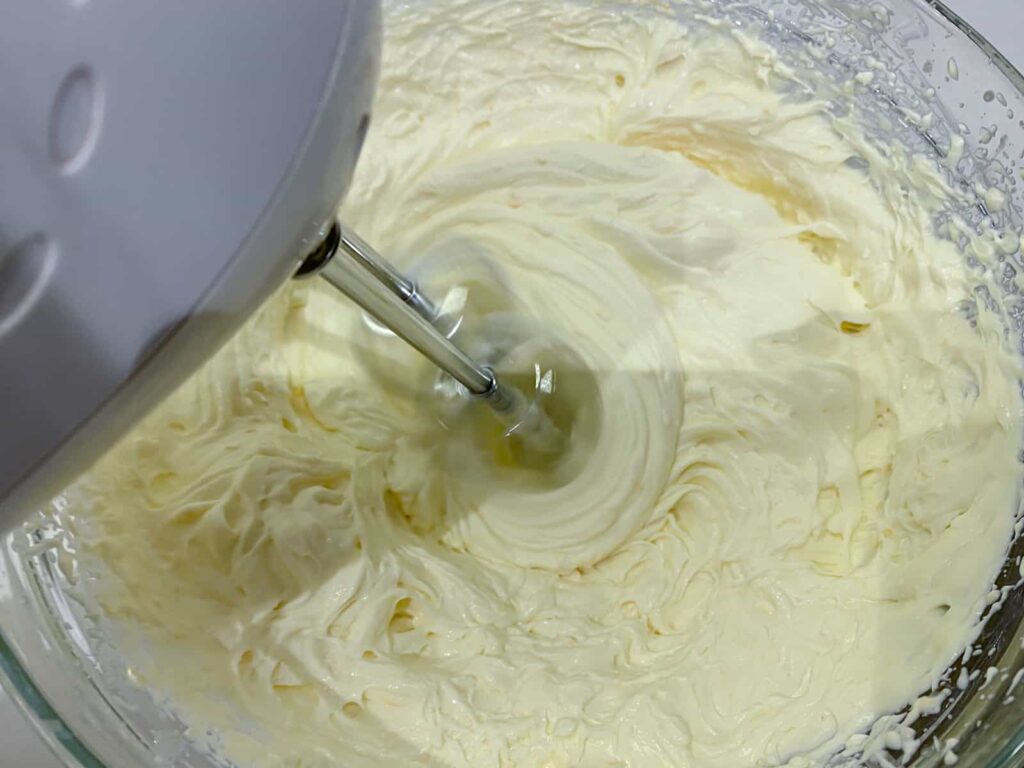 Whisking double cream with a hand mixer in a glass bowl.