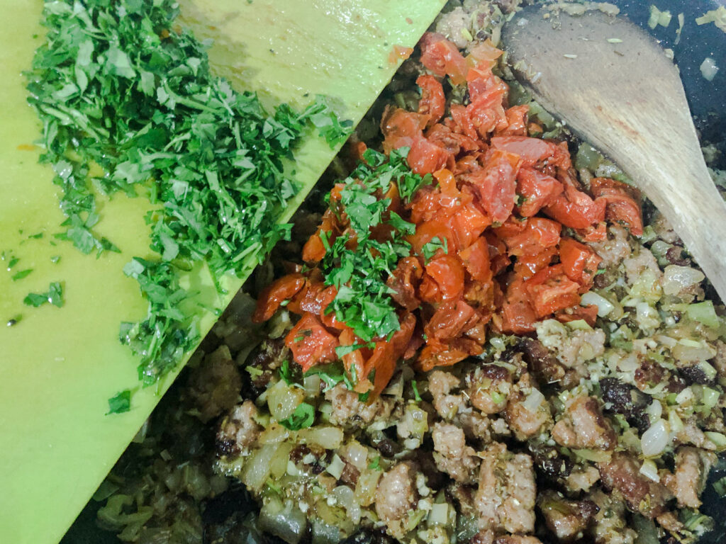 Adding fresh chopped herbs to cooked minced sausage.
