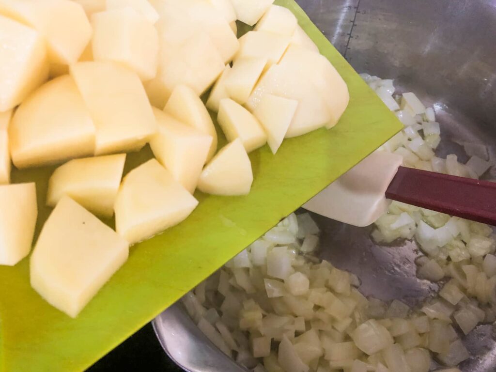 Adding cubed potatoes to onions that have been sauteed until soft in a pan for the base of soup.