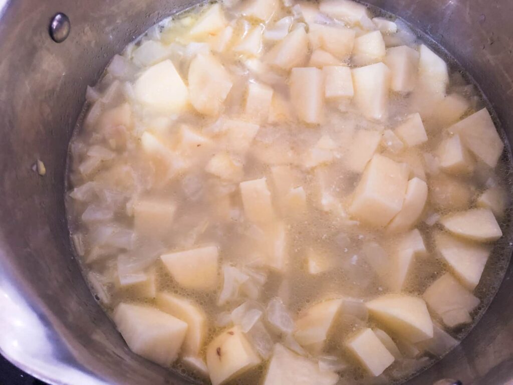 A pan of cooked onions and potatoes simmering in stock.