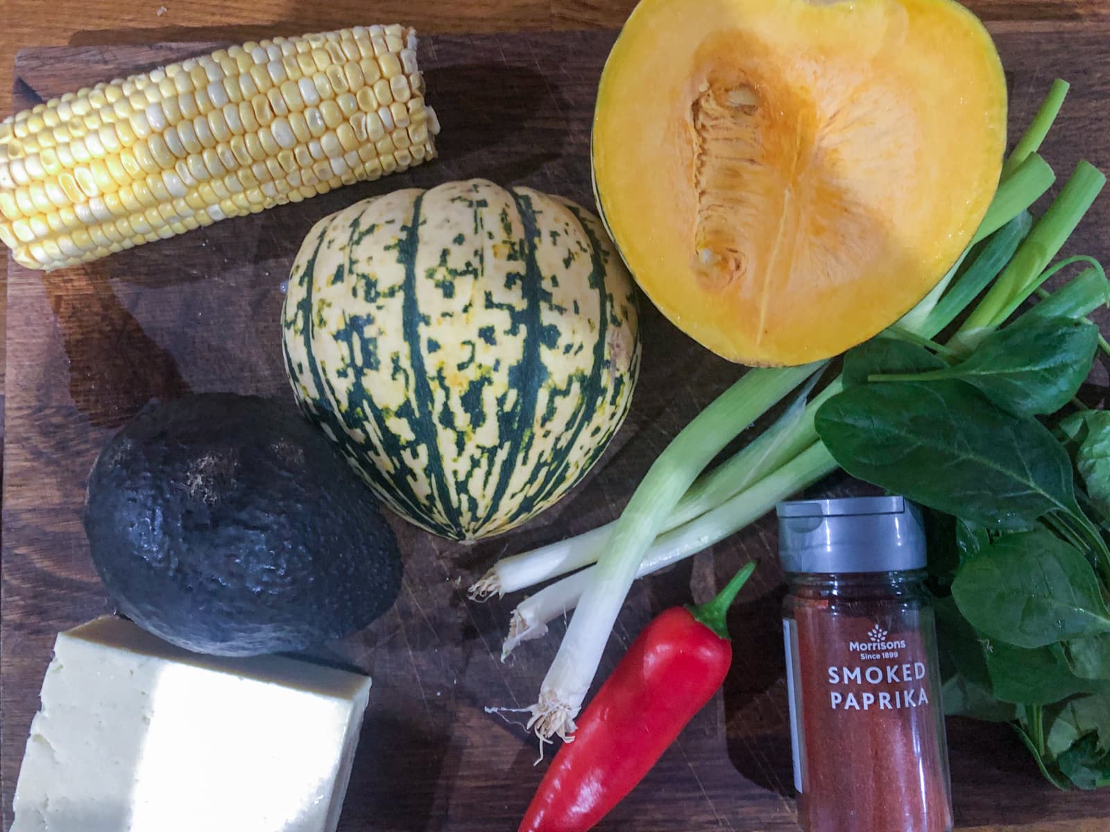 Various small pumpkins with spring onions, chillies, avocado, corn and smoked paprika on a wooden chopping board.