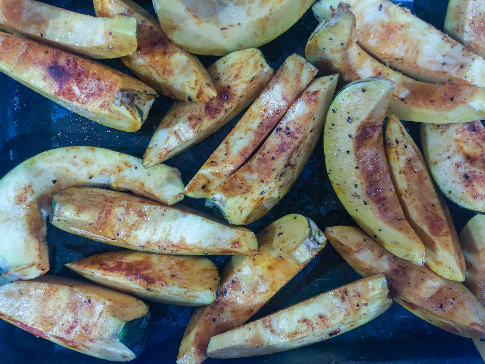 Wedges of pumpkins tossed with smoked paprika on a baking tray.