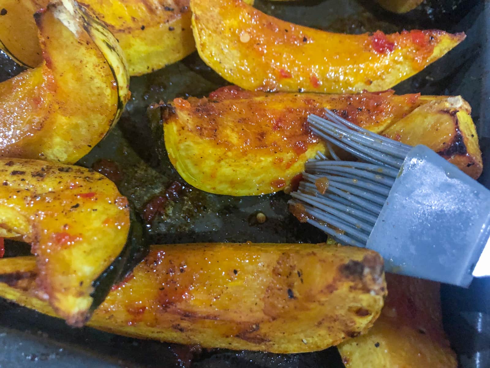 Roasted pumpkin wedges being brushed with chilli jam at the end of the cooking process.