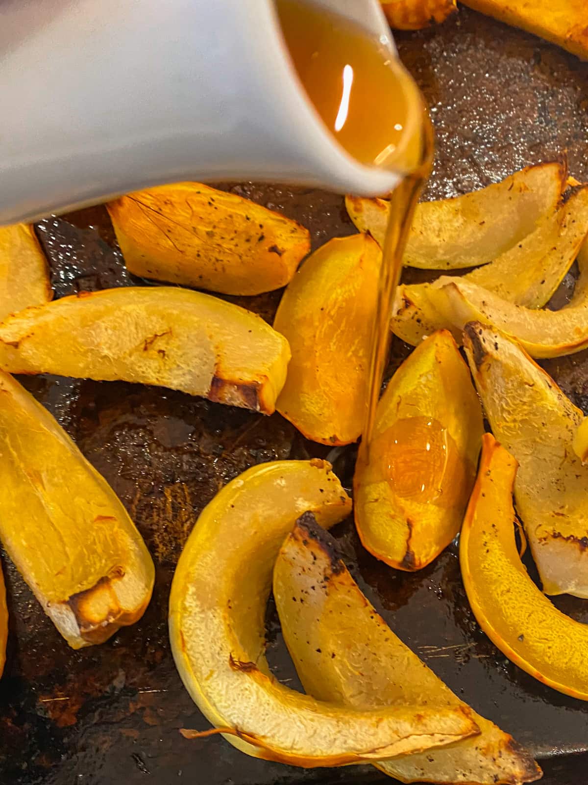 Wedges of roasted pumpkin drizzled with maple syrup on a metal roasting tray.