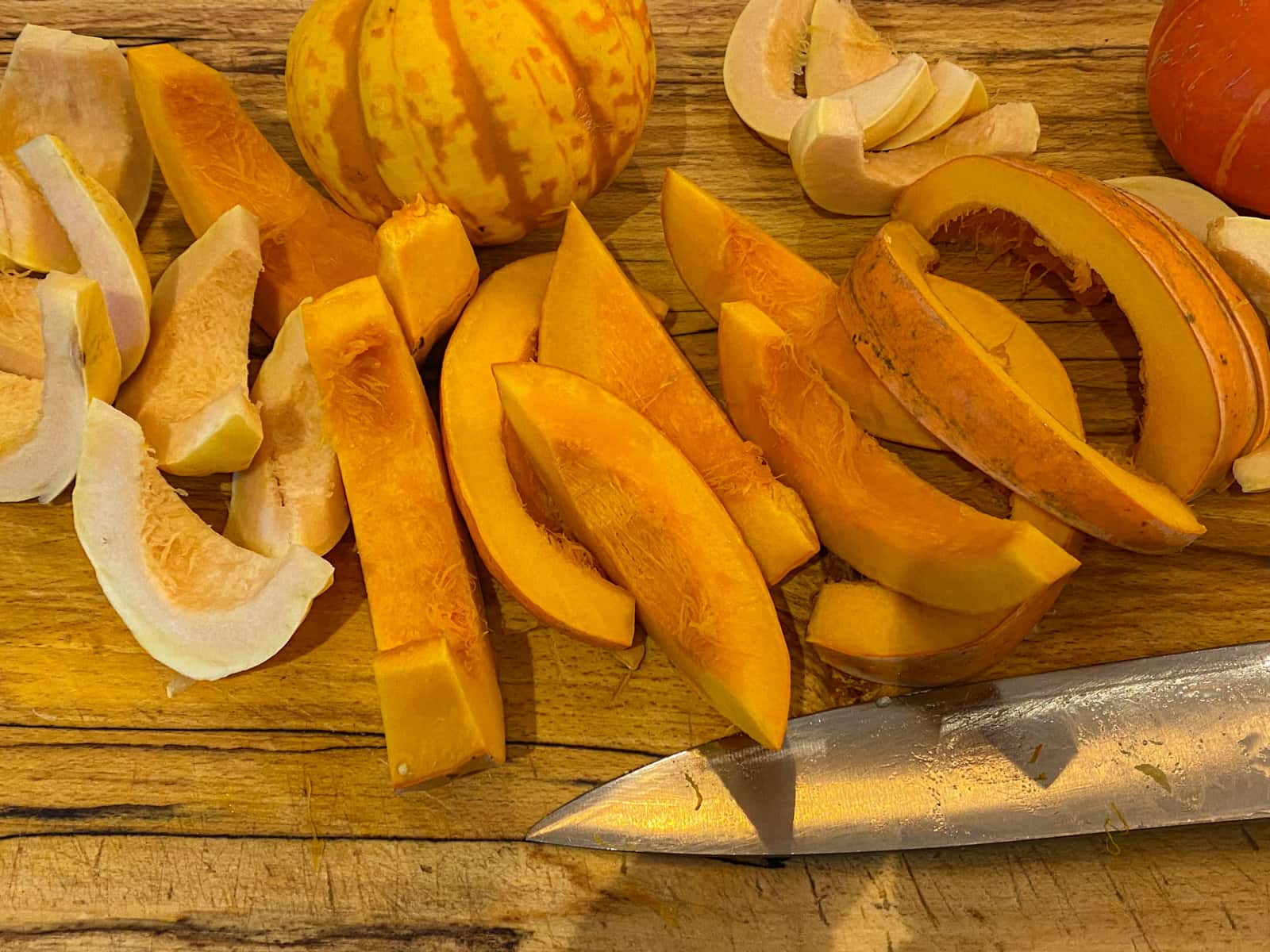 Pumpkins cut into wedges on a wooden board with a large chef's knife to the front.