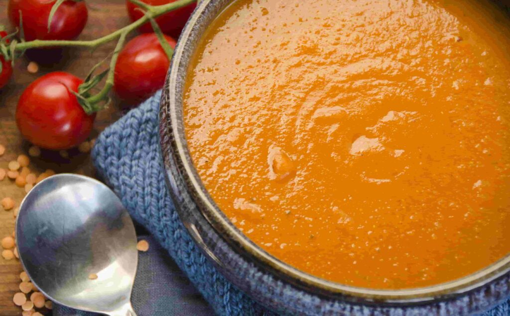 Spicy tomato lentil soup in a blue pottery bowl on a blue knitted napkin.