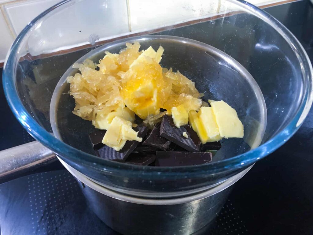 Butter, dark chocolate and ginger melting in a glass bowl over a water bath.