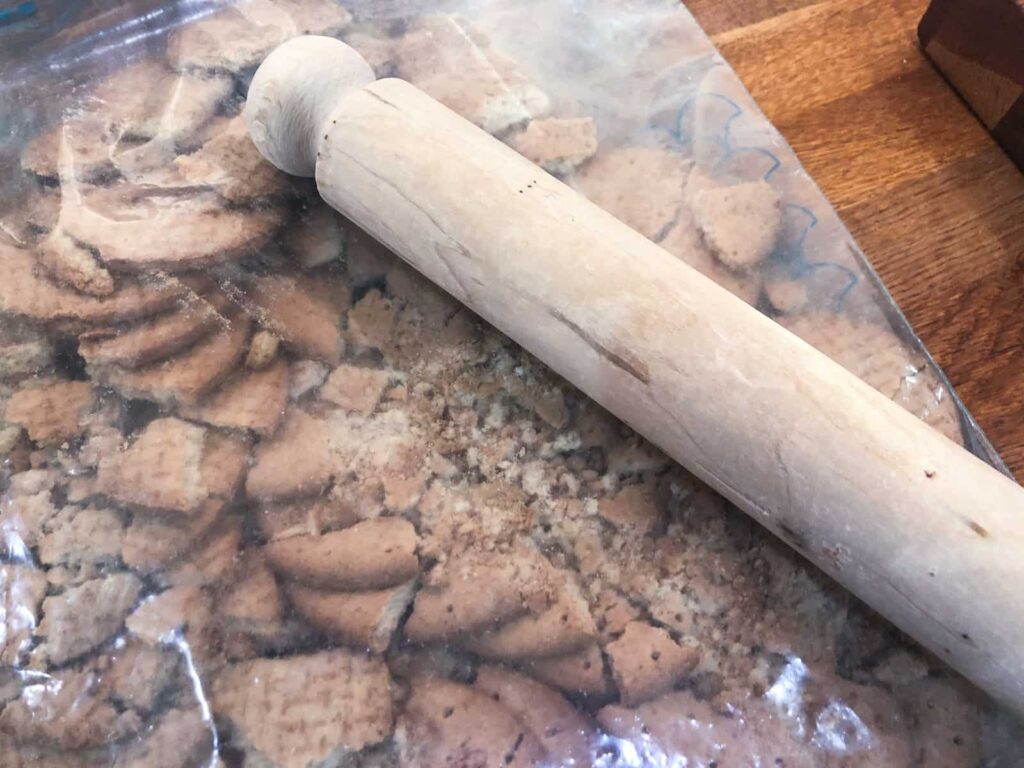 Crushing digestive biscuits with a rolling pin in a plastic bag.