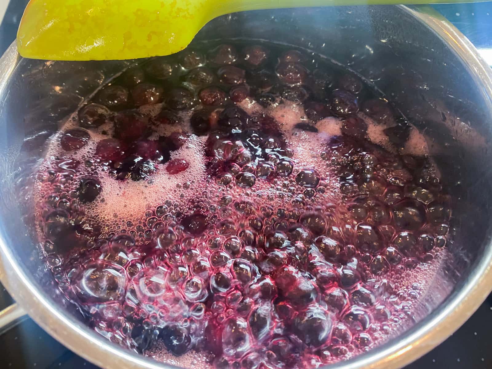 Blueberries, water and sugar at a rolling boil stage in a small pan.