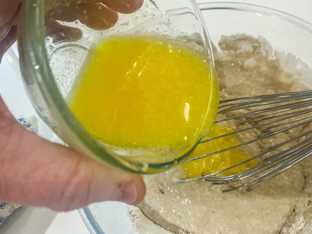 Melted butter being added to a thick buttermilk pancake mixture.