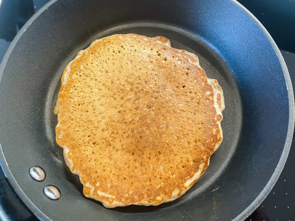 A large buttermilk pancake in a frying pan after being flipped and fully cooked on the top.