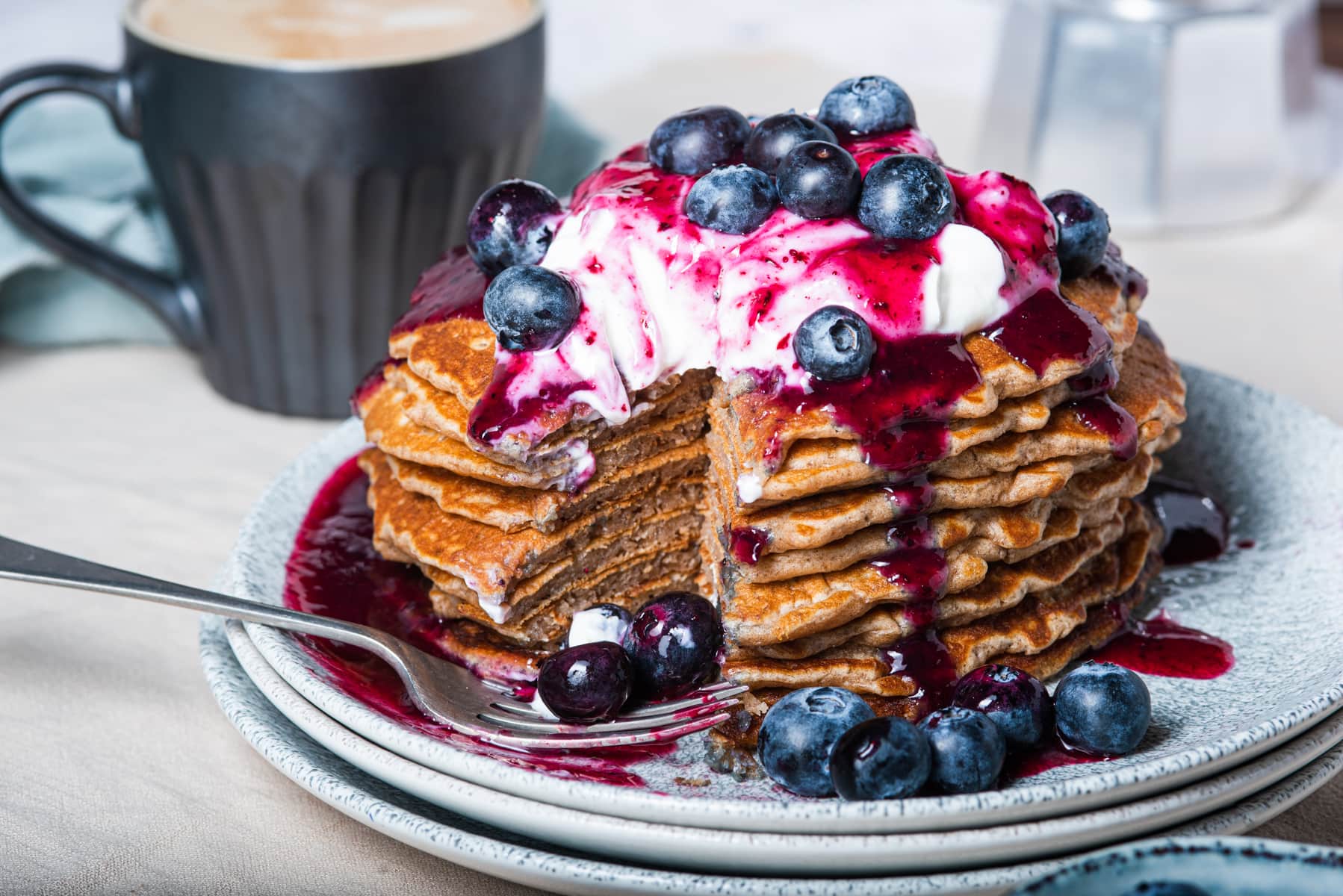 A stack of buttermilk pancakes topped with vanilla yogurt, fresh blueberry syrup and lots of fresh blueberries.