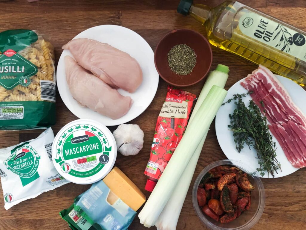 Ingredients including chicken breasts, cheese, bacon, herbs and tomatoes to make a delicious pasta dish.