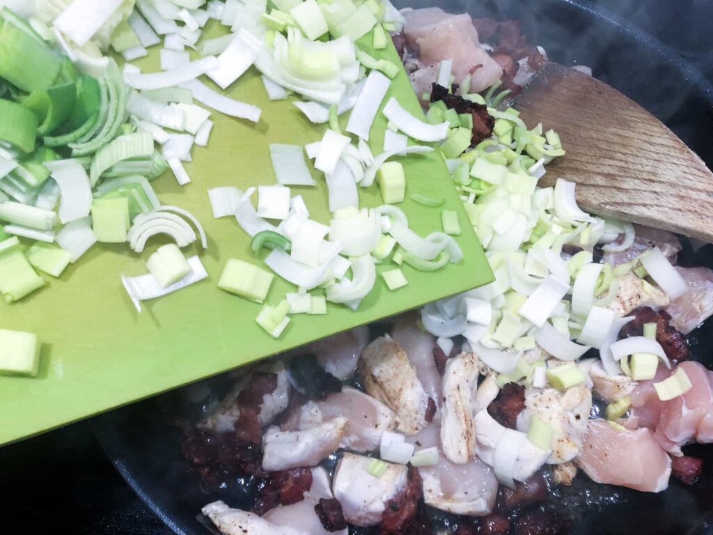 Fresh sliced leeks being added to pan fried chicken and bacon pieces.
