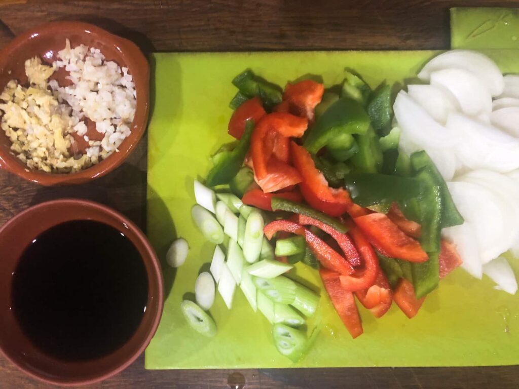Vegetables chopped on a green chopping board with prepped sauce and garlic mix to make a stirfry.