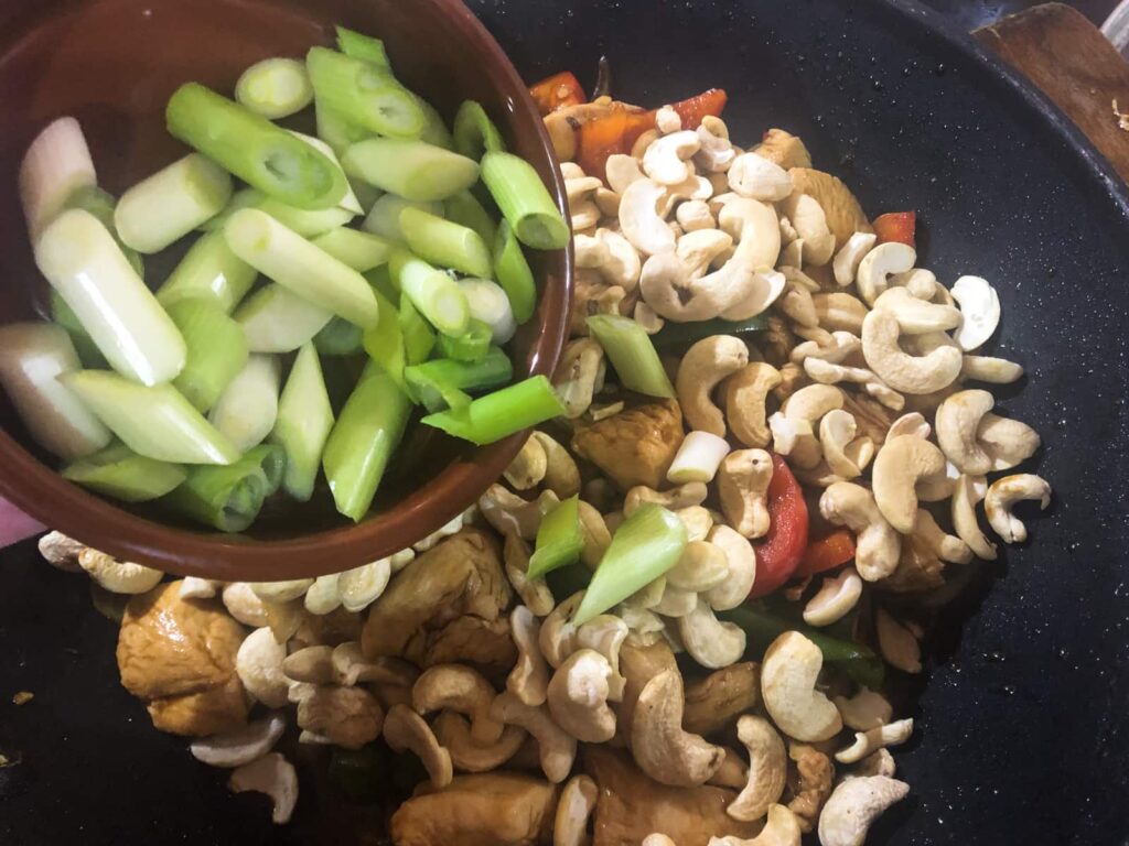 Adding chopped spring onions to a stir fry in a hot wok.