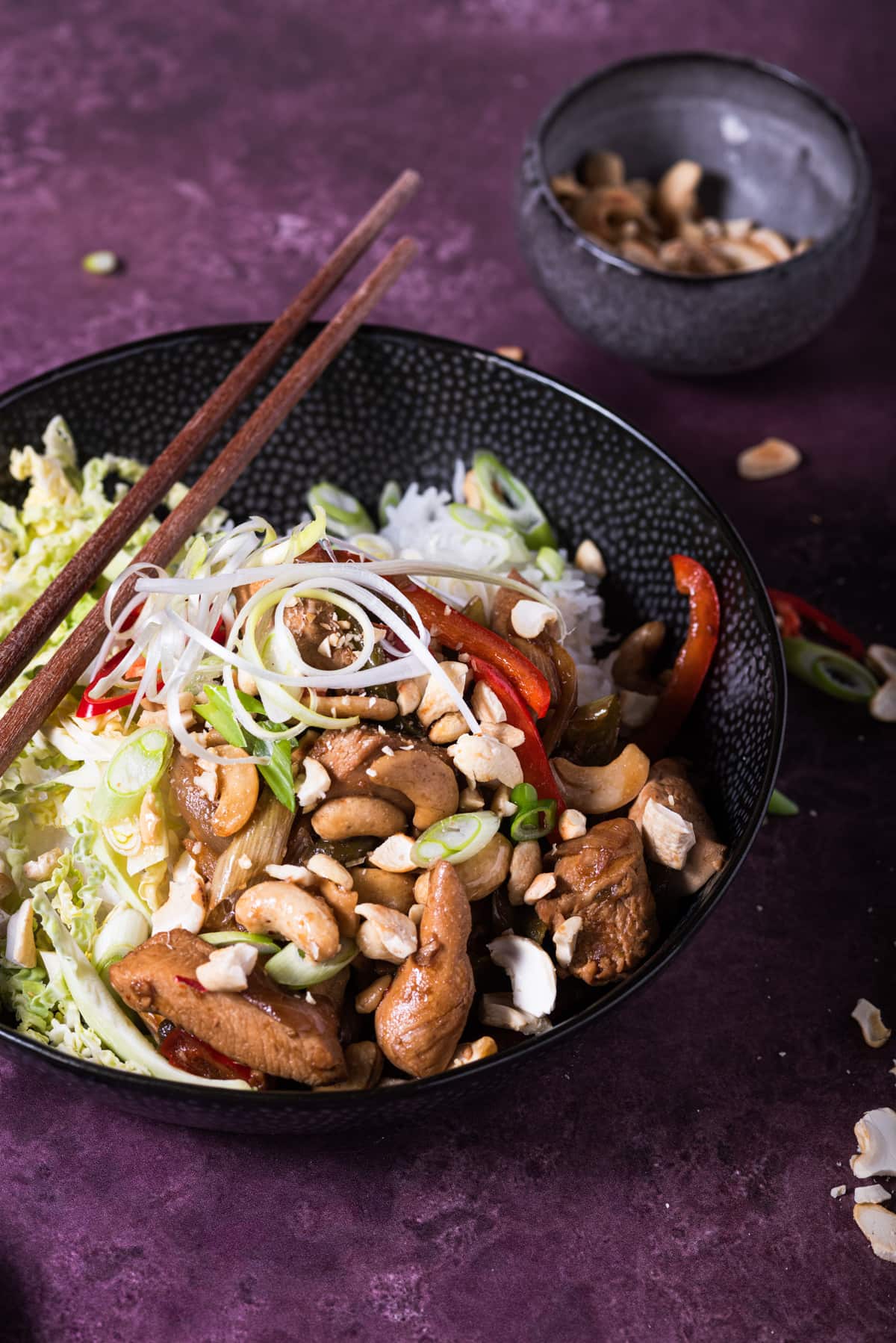 A delicious and tempting bowl of chicken and cashew nut stirfry served with sliced chillies and chopsticks.