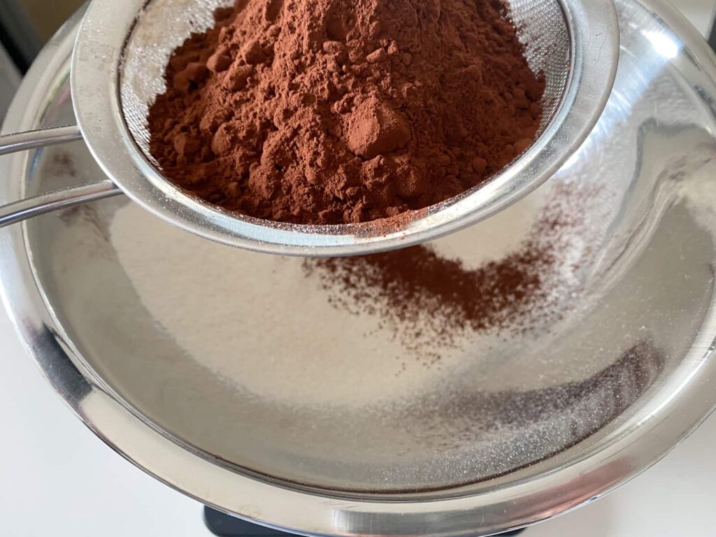 Sieving cocoa powder and flour into a bowl through a fine mesh sieve.