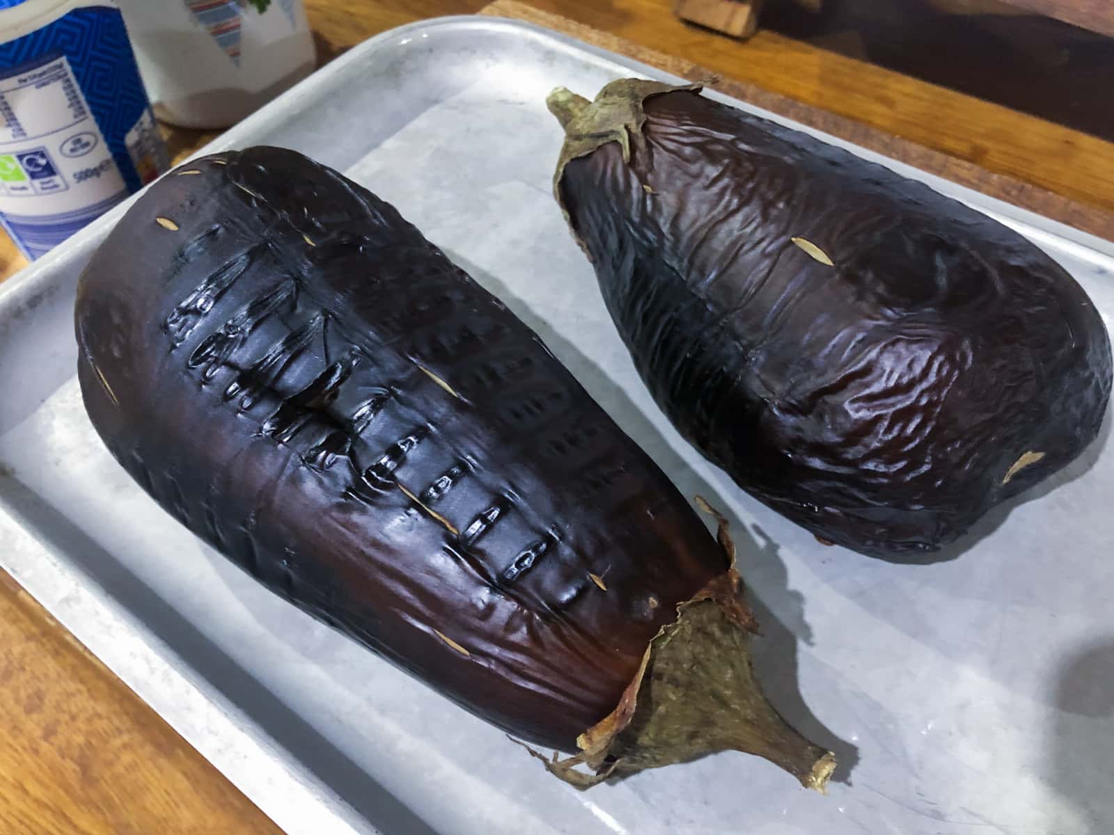 Two large aubergines (eggplants) pierced with a knife and baked on a baking sheet.