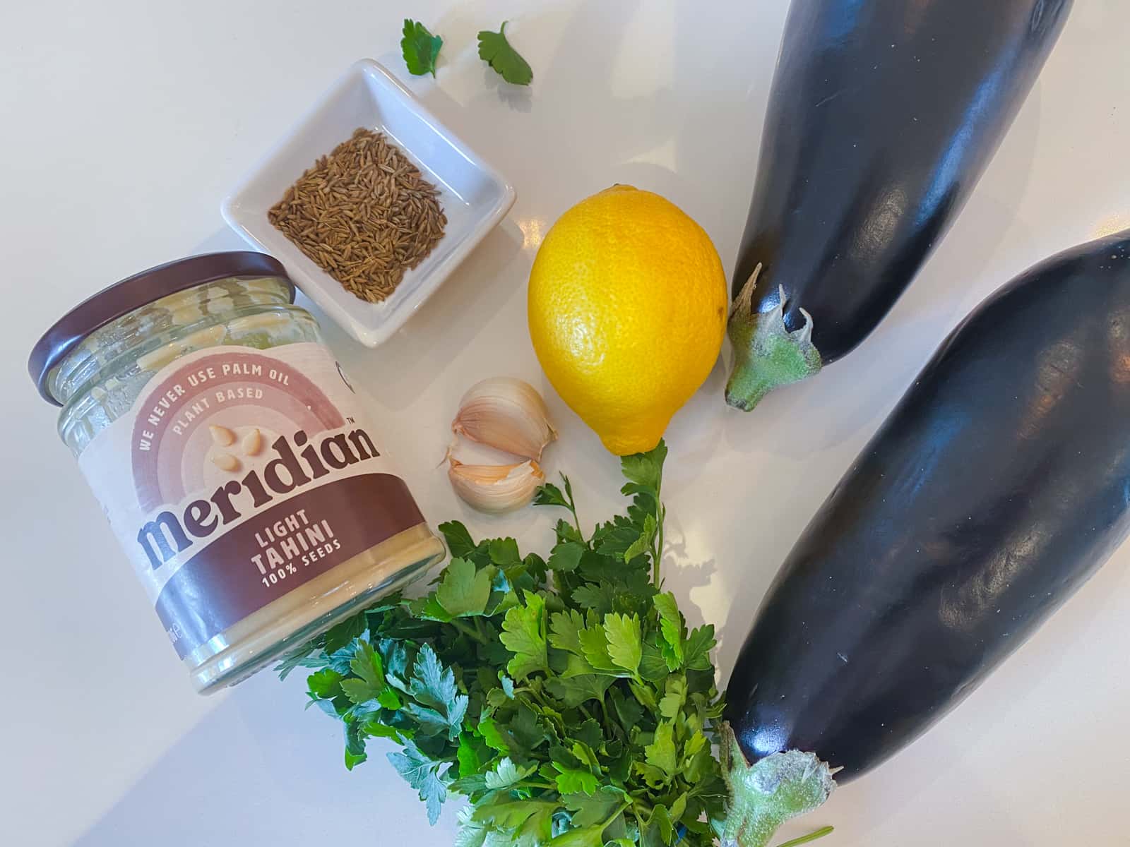 Tahini, parsley, lemon, garlic, cumin seeds and aubergine - ingredients to make a baba ganoush dip.