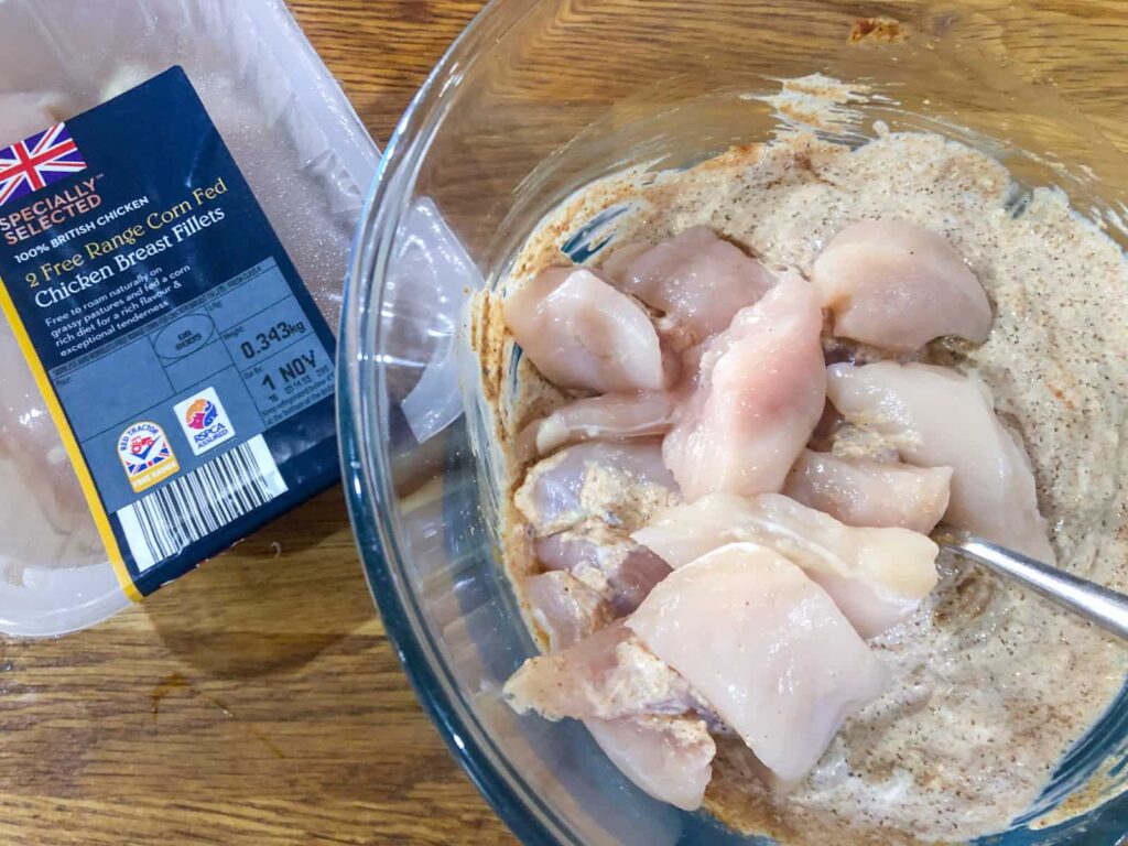 Chicken pieces being marinated in a glass bowl.