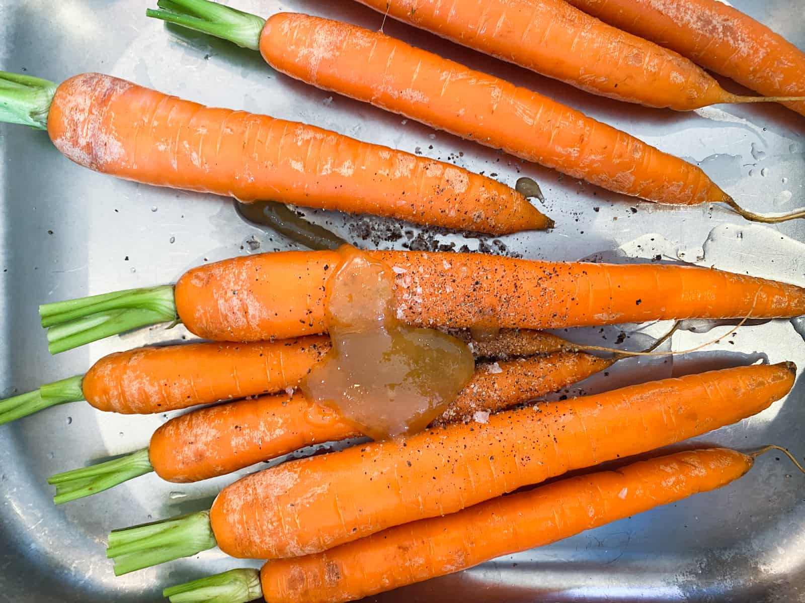 Fresh carrots with tops still in tact with honey, salt, pepper and cumin about to be roasted.
