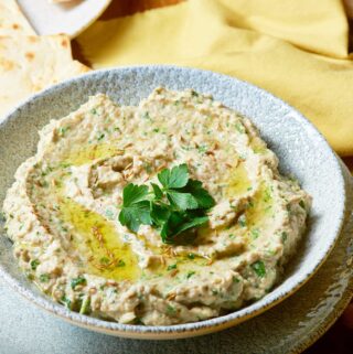 A delicious and fresh baba ganoush dip topped with parsley in a mottled grey serving dish.