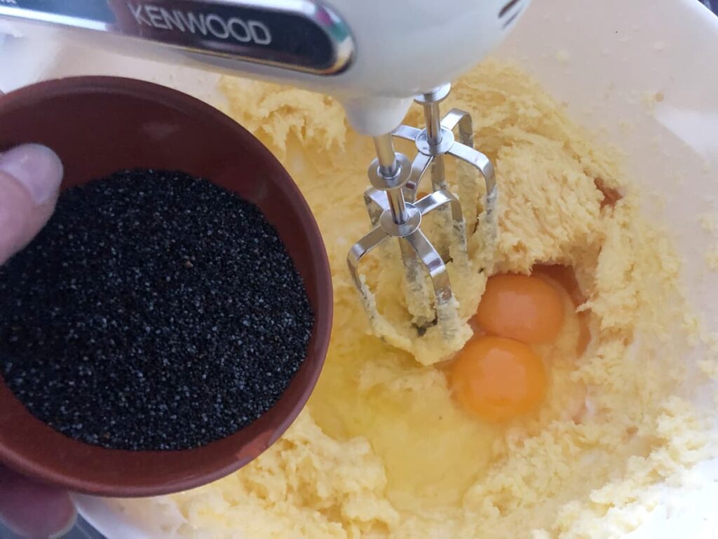 Poppy seeds being added to a creamed butter and sugar mix along with fresh eggs.