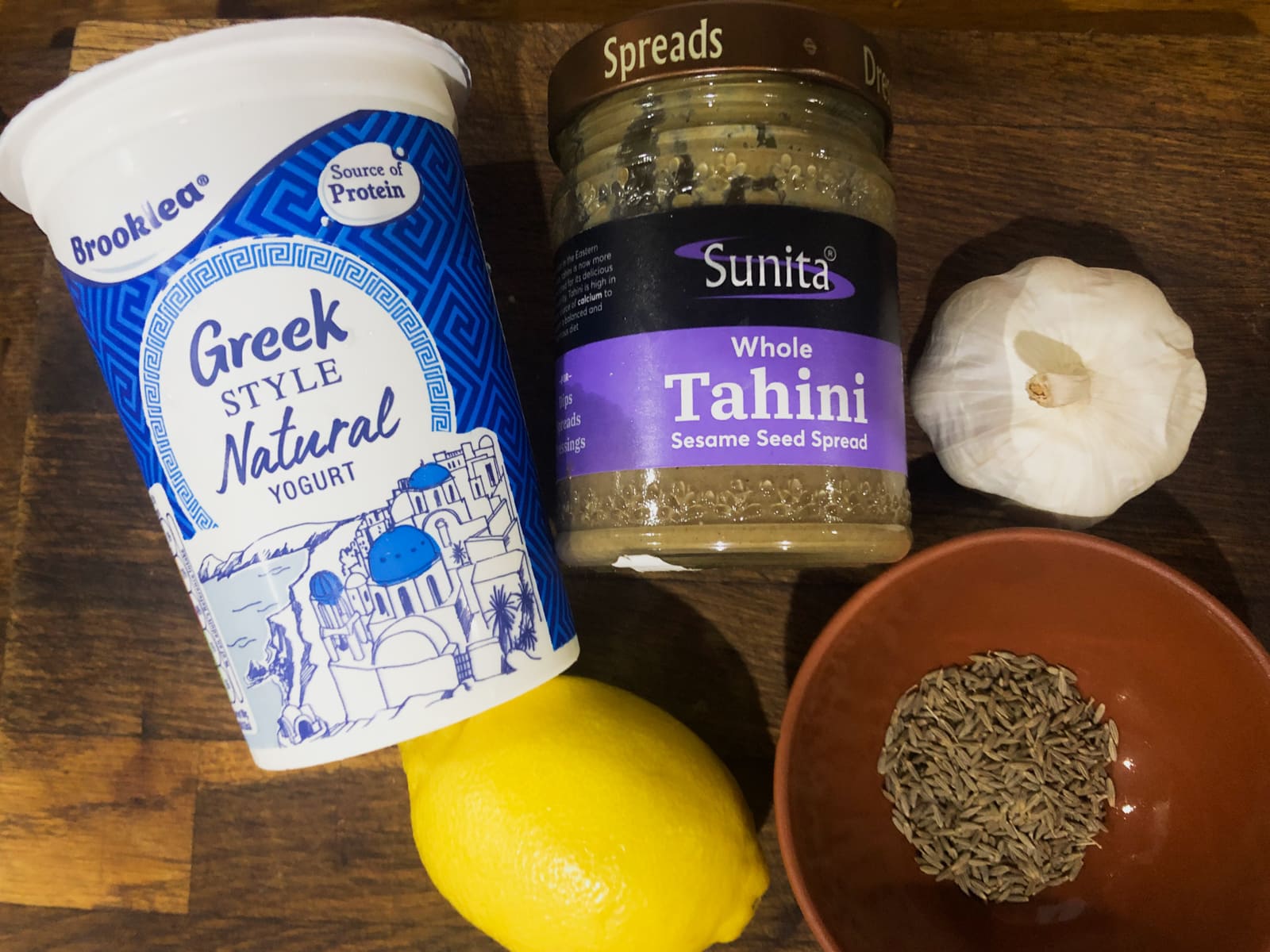 Ingredients to make lemon and tahini dressing, including lemons, yogurt, tahini, garlic and toasted cumin seeds.