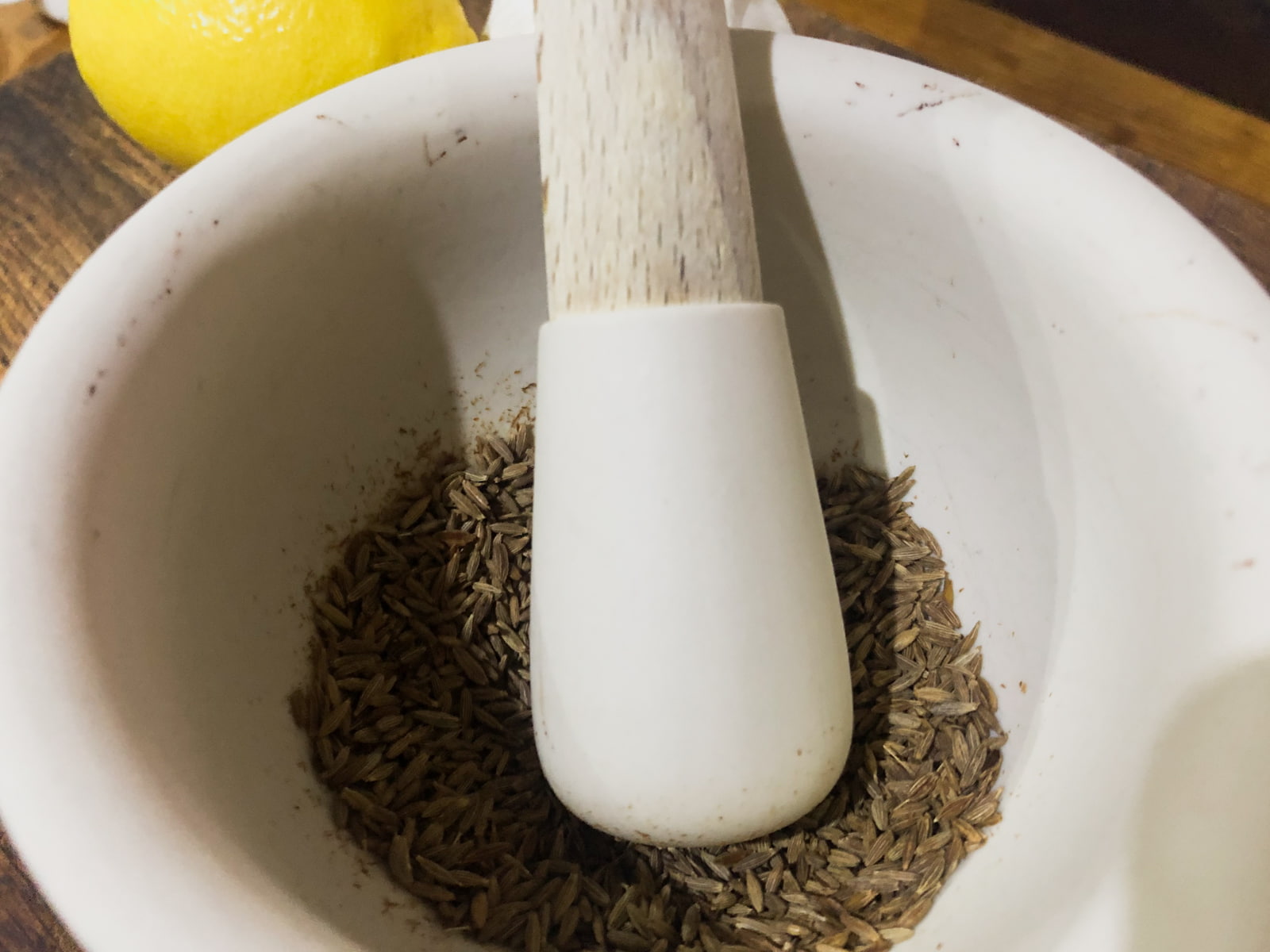 Crushing toasted cumin seeds in a pestle and mortar.
