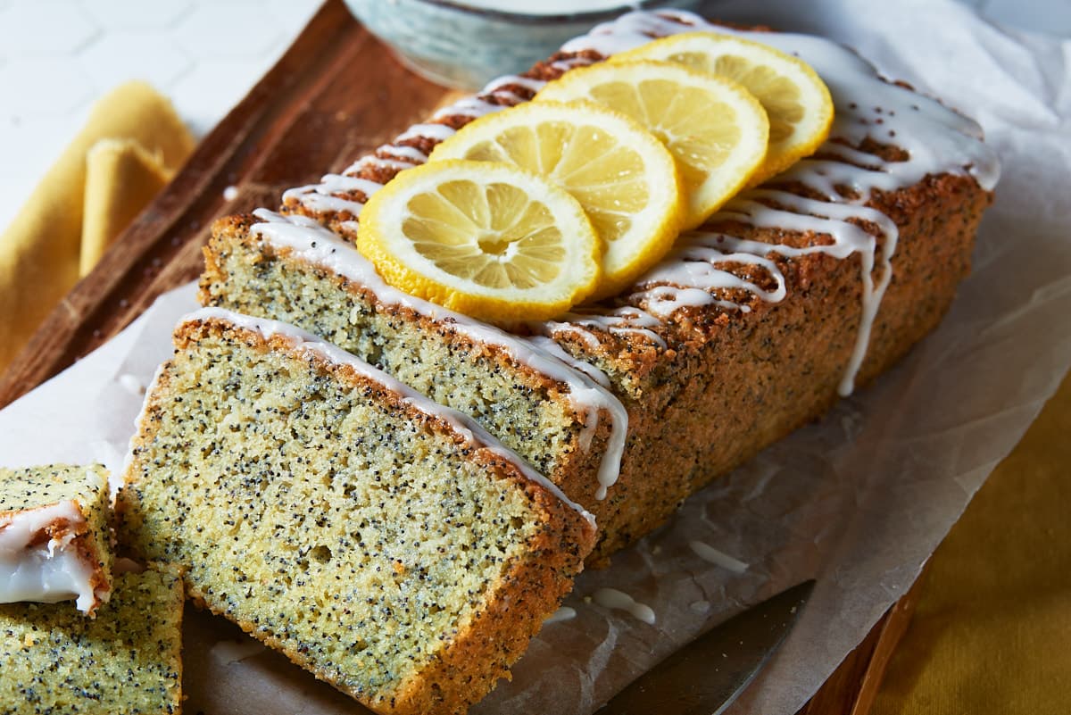 A lemon and poppyseed cake topped with slices of fresh lemon on a wooden chopping board drizzled with a thin layer of icing.
