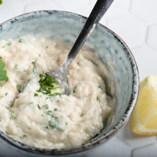 A creamy horseradish dressing in a blue mottled bowl with a wedge of lemon alongside.
