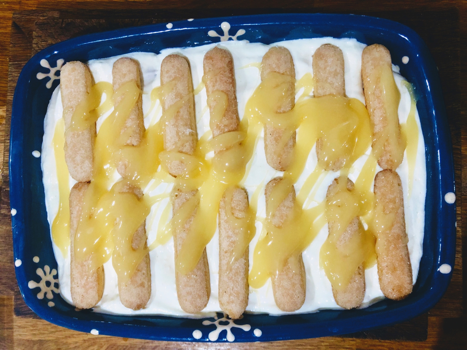 Large dish filled with lemon mascarpone cream topped with sponge fingers and a drizzle of lemon curd