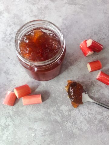 Jar of rhubarb and ginger jam with a spoon of jam and slices of rhubarb alongside