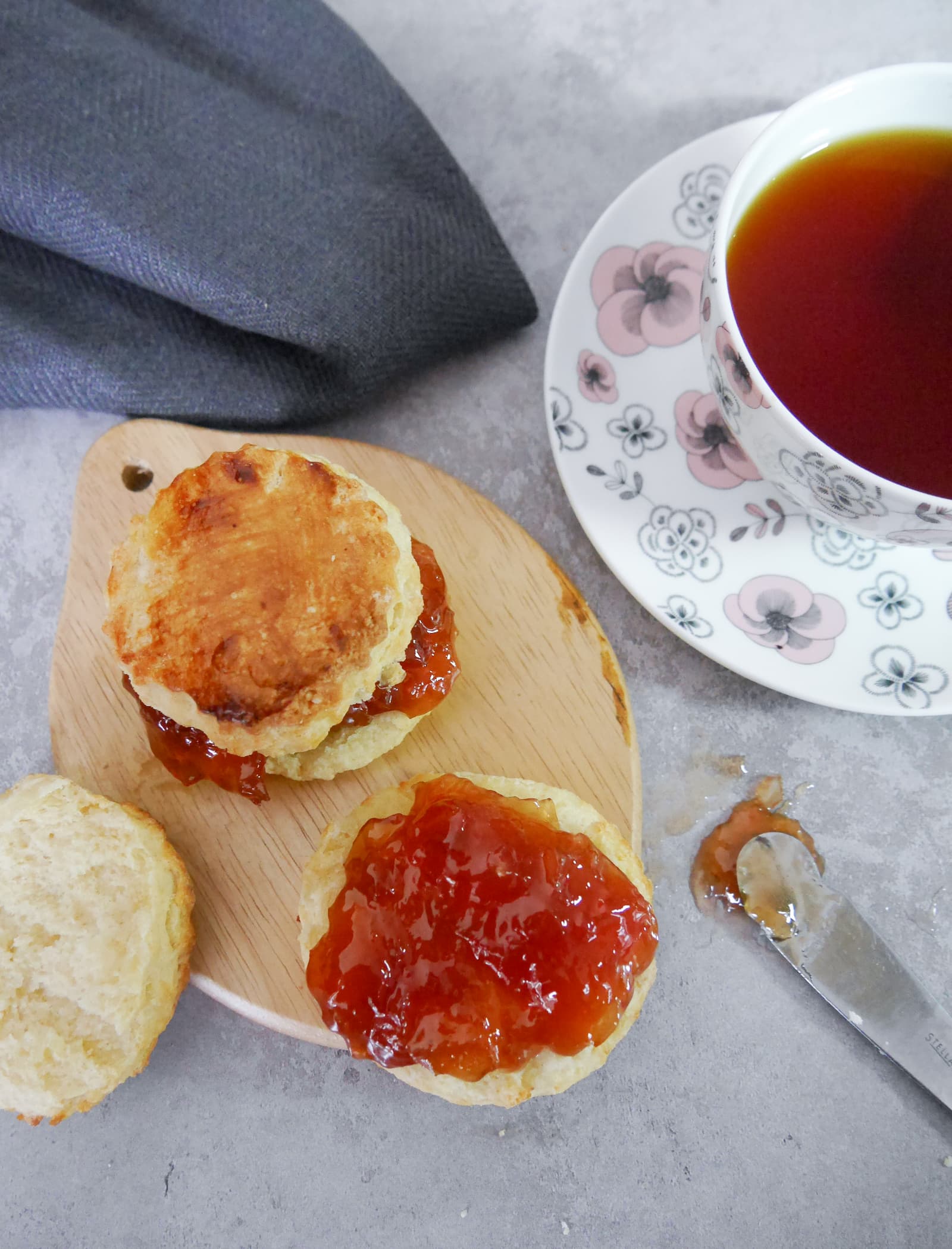 Two scones set filled with rhubarb jam and set on a wooden board, with a cup of tea alongside