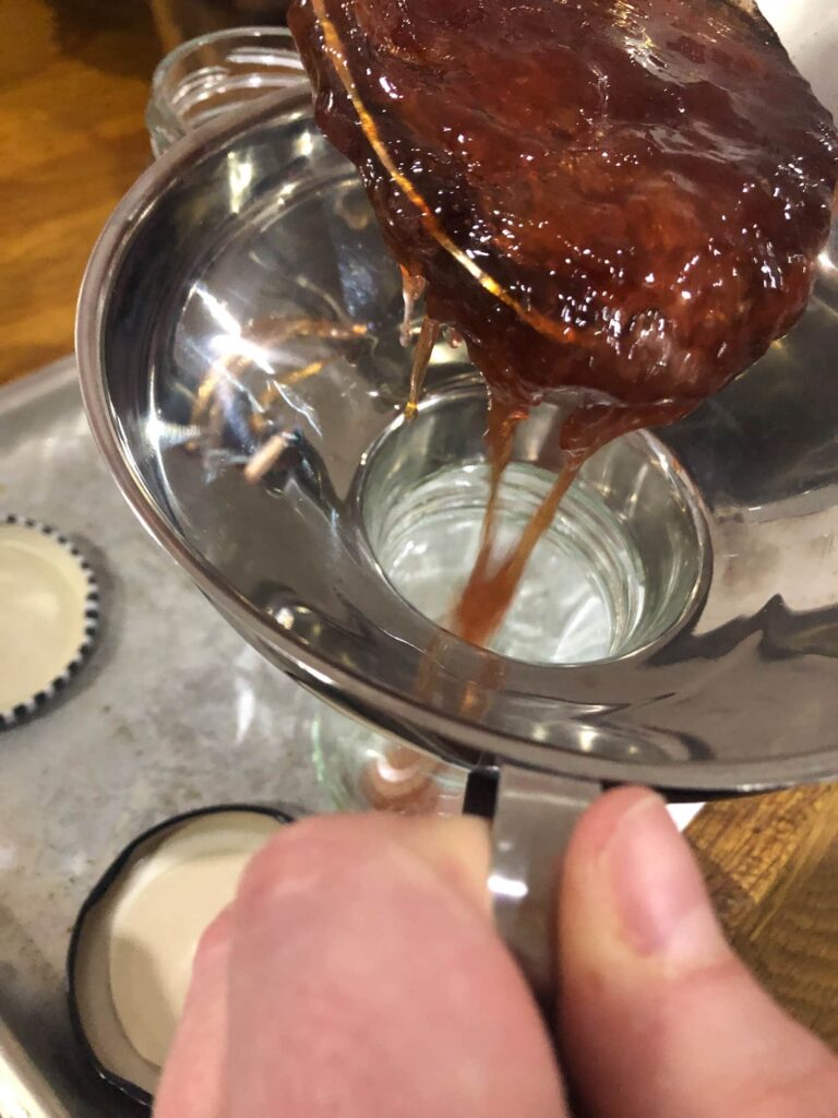 Ladle of hot jam being poured through a jam funnel into a glass jar