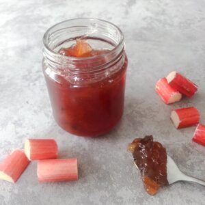 Jar of rhubarb and ginger jam with a spoon of jam and slices of rhubarb alongside